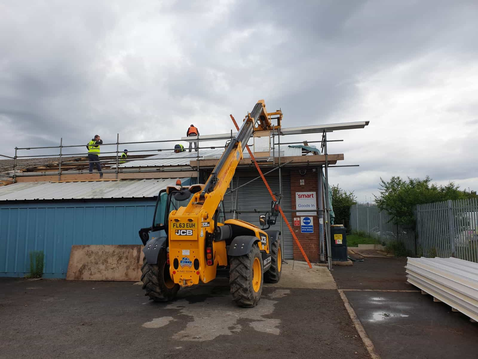 Machinery demolishing a roof that also has scaffolding on it