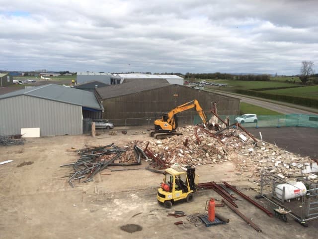 Diggers carrying out a site clearance in front of a hangar with a pile of rubble in front of them