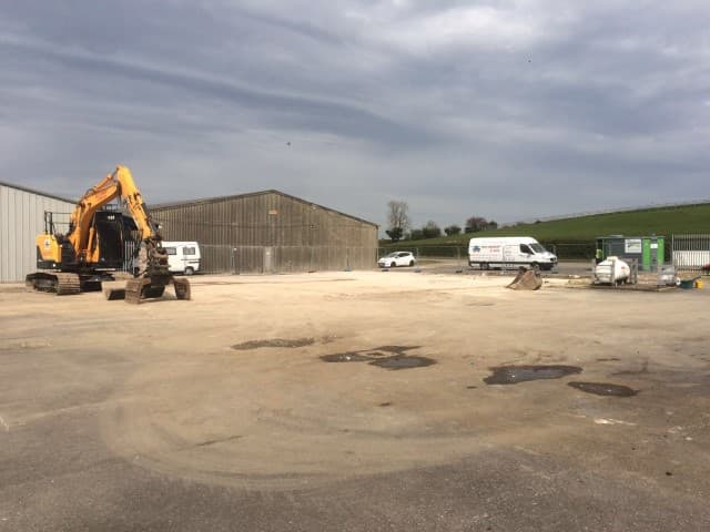 Digger in front of a hangar with two vans in view