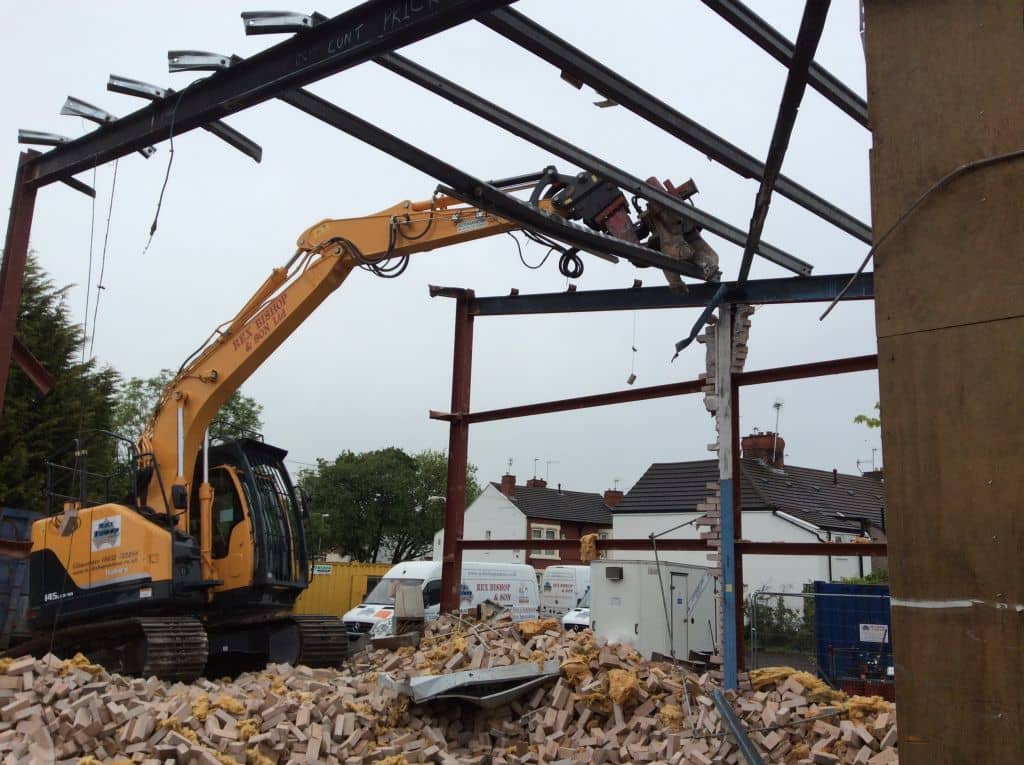 Digger on a pile of rubble tearing a roof down